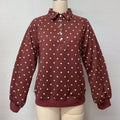A long-sleeve collared pullover top in a rust brown color with white polka dots, displayed on a beige dress form mannequin against a plain white wall.