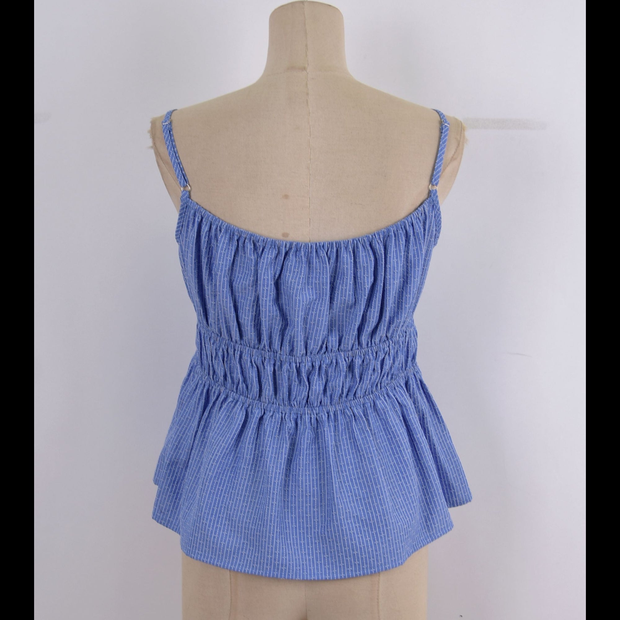 A blue and white gingham patterned camisole top with a smocked waist and thin shoulder straps, displayed on a beige fabric mannequin torso against a white background.