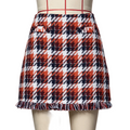 A plaid mini skirt with fringe hem displayed on a mannequin. The pattern features red, navy blue, and white diagonal plaid blocks.