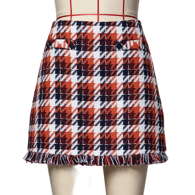 A plaid mini skirt with fringe hem displayed on a mannequin. The pattern features red, navy blue, and white diagonal plaid blocks.