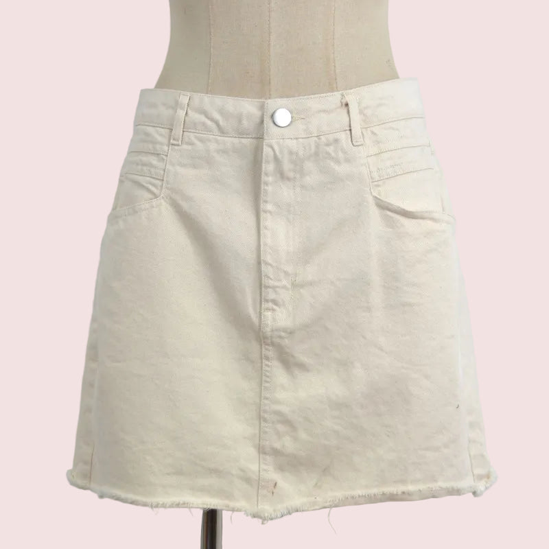 A light beige denim mini skirt with a raw, frayed hem, displayed on a cream-colored dress form mannequin against a plain light gray background.