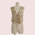 A sleeveless beige vest with a deep V-neck and tie-front closure, decorated with large cream floral embroidery, displayed on a beige dress form against a light gray background.