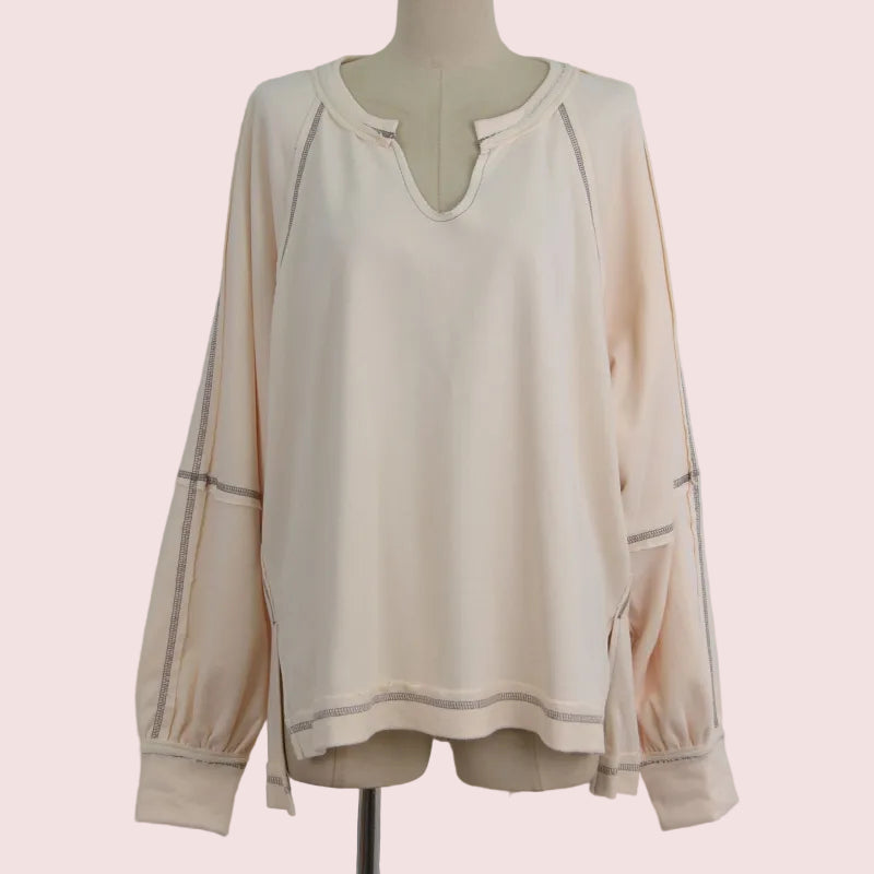 A cream-colored long-sleeve blouse with a split V-neckline and subtle contrast stitching, displayed on a dress form mannequin against a light gray background.