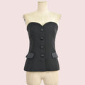 A black strapless corset-style top with a sweetheart neckline, four front buttons, and two flap pockets, displayed on a cream dress form against a white background.
