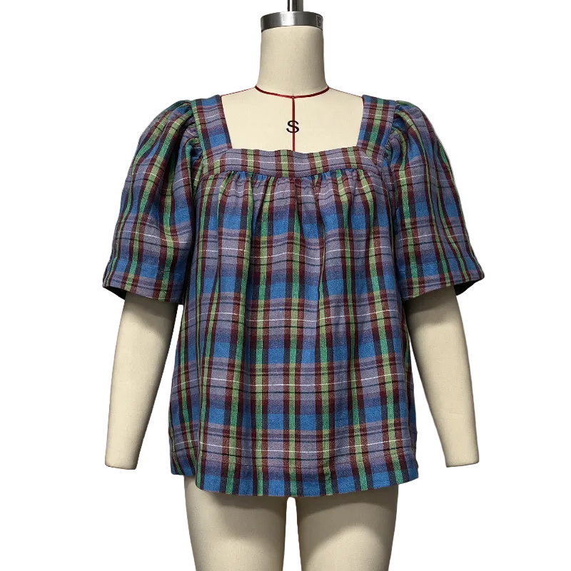A plaid puff-sleeve top displayed on a cream mannequin torso against a plain light gray wall. The top has a square neckline, smocked upper chest, and a multicolor tartan pattern with blue, purple, green, and red tones.