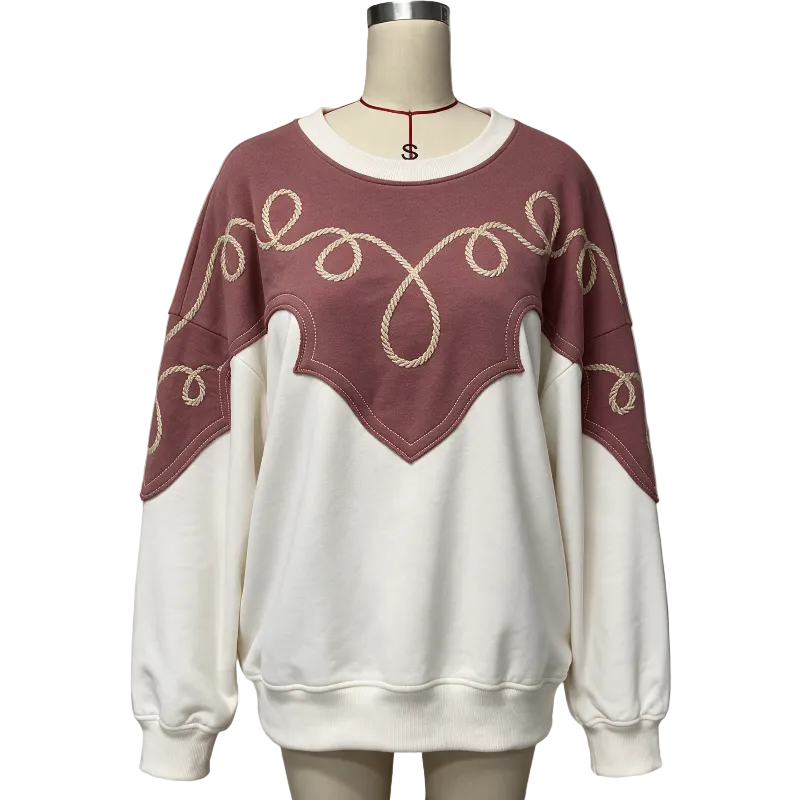 A crewneck sweatshirt displayed on a mannequin, featuring a dusty rose upper section with cream rope-like embroidered swirl patterns across the shoulders and chest, and an off-white lower body and sleeves.