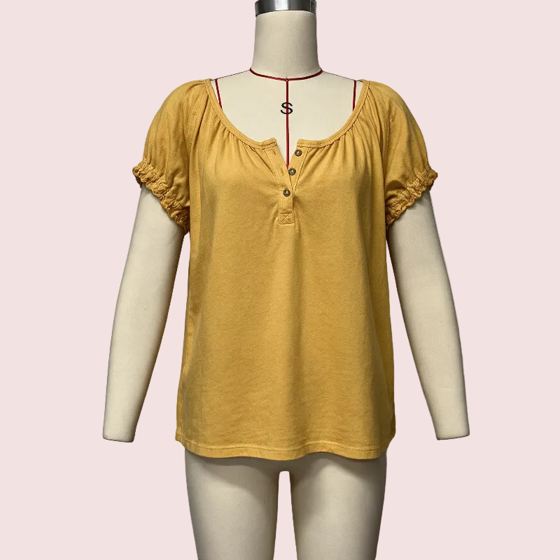 A mustard yellow short-sleeve henley top displayed on a cream mannequin against a pale pink background.