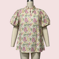 A short-sleeve blouse with a high mock neck and puff sleeves, featuring a pink and green floral print on a cream background, displayed on a mannequin.