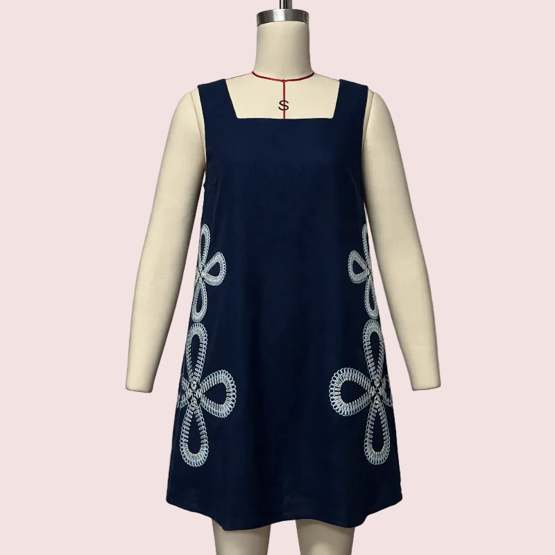 A sleeveless navy blue dress displayed on a cream mannequin torso, featuring white floral knot embroidery on the front and a red cord detail at the neckline.