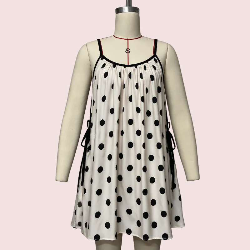A sleeveless white slip dress with black polka dots and thin black straps, displayed on a cream mannequin against a pale pink background.