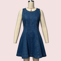 A sleeveless blue denim dress displayed on a cream mannequin against a pale pink background. The dress has a round neckline, a front center seam, and a flared skirt.