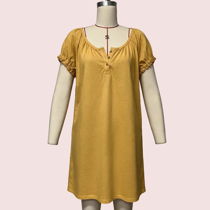 A mustard yellow short-sleeve nightgown with a scoop neckline, decorative buttons, and ruffled cuffs, displayed on a cream-colored dress form mannequin against a solid pale pink background.