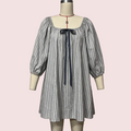 A sleeveless puff-sleeve dress with vertical gray and white stripes, featuring a square neckline with a dark blue bow detail, displayed on a cream-colored mannequin against a solid pale pink background.