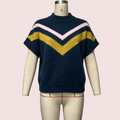 A short-sleeve knit sweater displayed on a cream mannequin torso against a pale pink background. The sweater is navy blue with a large mustard yellow V-stripe across the chest and a thinner light pink V-stripe above it.