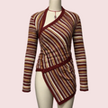A long-sleeve wrap-style top displayed on a mannequin torso against a plain light gray wall. The garment has horizontal multicolor stripes with a deep burgundy base and warm tan, cream, and rust tones throughout.