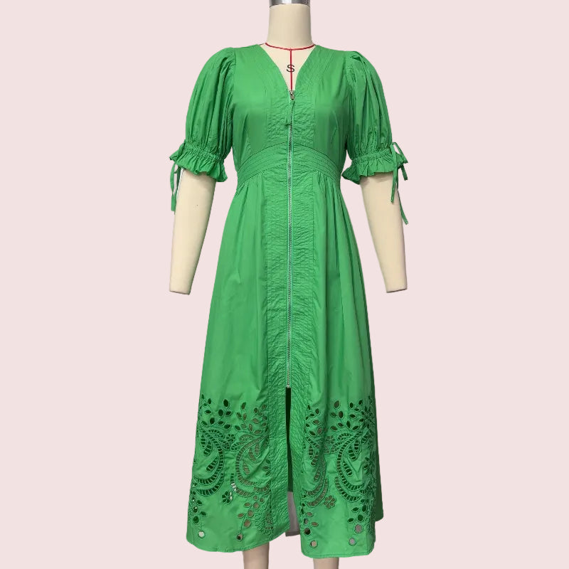 A bright green midi dress with puff sleeves, a front zipper, and eyelet embroidery near the hem, displayed on a cream mannequin against a plain white wall.