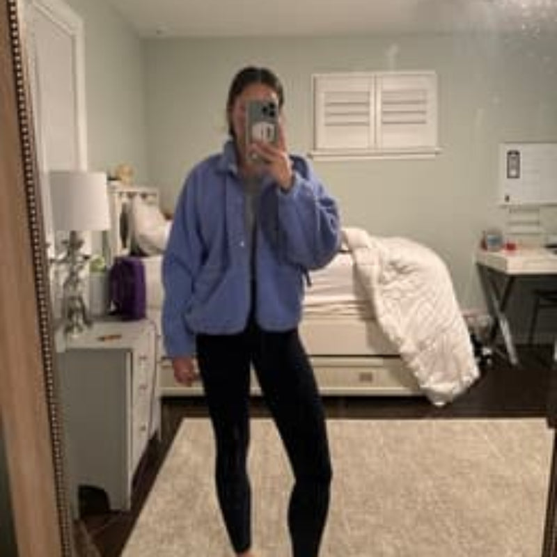 Person taking a mirror selfie in a bedroom wearing a blue sweatshirt and black pants.