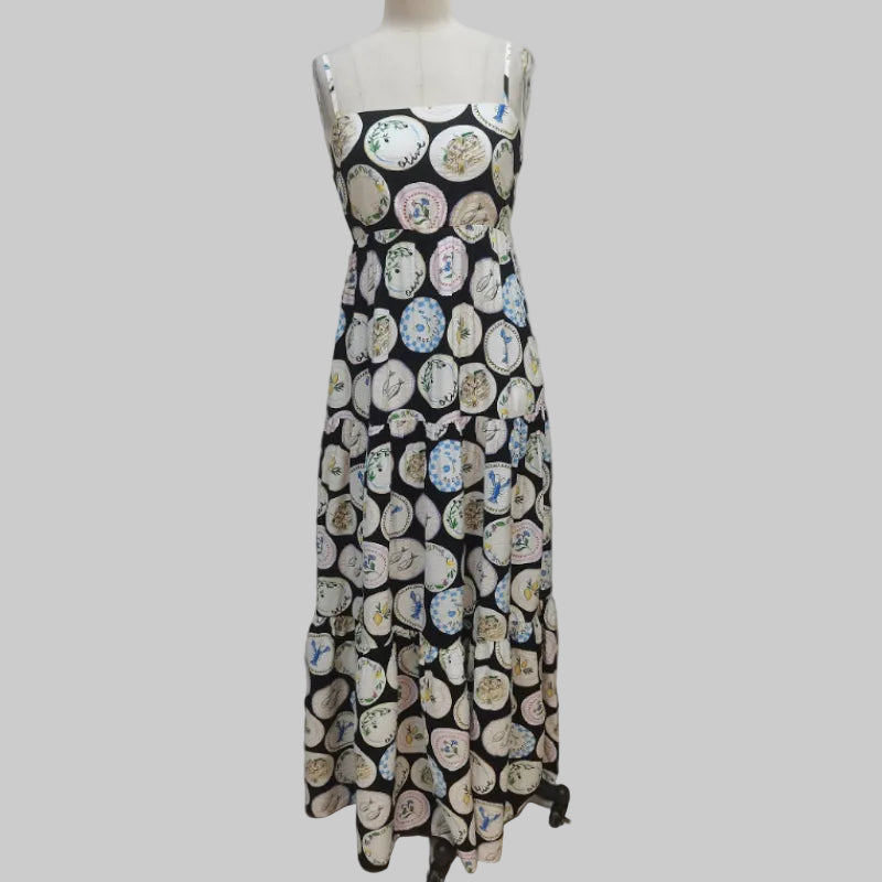 A sleeveless black maxi dress with a tiered ruffle skirt, featuring an all-over print of circular plates with colorful floral and decorative motifs. The dress is displayed on a mannequin against a plain white backdrop.
