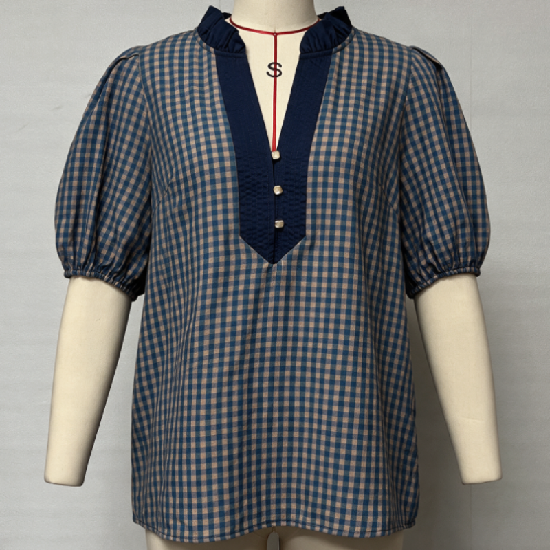 A blue and beige gingham short-sleeve blouse with a dark blue mock neck and button placket, displayed on a cream mannequin torso against a light gray background.