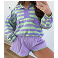 A person wearing a matching two-piece lounge set with lavender and light green horizontal stripes, featuring a long-sleeve button-front top and shorts with a thin green trim.