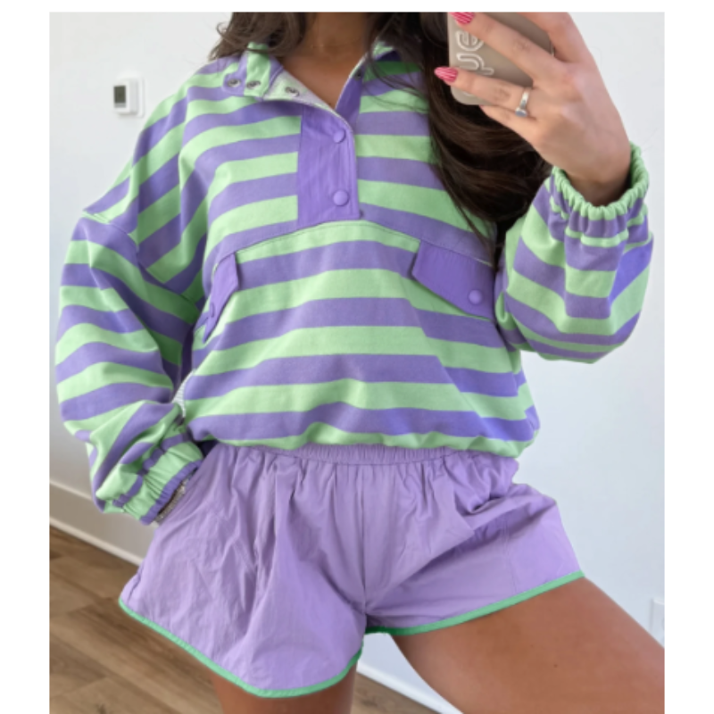 A person wearing a matching two-piece lounge set with lavender and light green horizontal stripes, featuring a long-sleeve button-front top and shorts with a thin green trim.