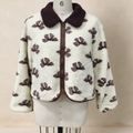 A cream-colored sherpa fleece jacket with a dark brown patterned leaf design and a dark brown collar, displayed on a white dress form mannequin.