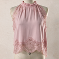 A sleeveless high-neck blouse in light pink, featuring floral lace trim along the neckline, armholes, and hem, displayed on a cream mannequin torso against a neutral beige background.