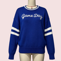 A royal blue knit sweater displayed on a cream mannequin torso. The sweater features 'Game Day' embroidered in white script across the chest and white athletic stripes on both sleeves.