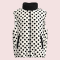 A sleeveless quilted vest with a black and white polka dot pattern, featuring a black stand-up collar, black front zipper, and zippered hand pockets, shown against a plain white background.