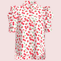 A white short-sleeve blouse with a red strawberry and cherry print, featuring ruffled shoulders and a pointed collar, shown on a plain white background.